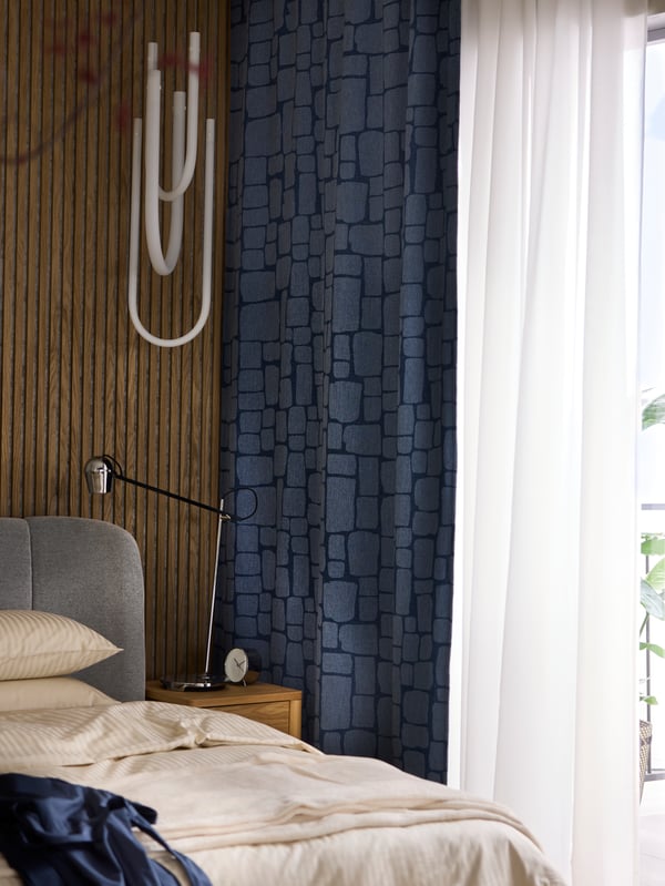 Gemütliches IKEA Schlafzimmer mit markanter Holzwand und stilvollem dunkelblauen Vorhang im Steinmuster – modernes Design trifft auf warme Materialien