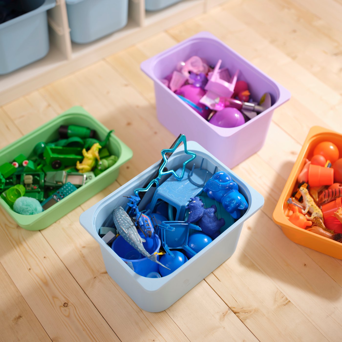 Four TROFAST storage boxes in different colours are placed on a floor. In each box there are toys matching the box’s colour.