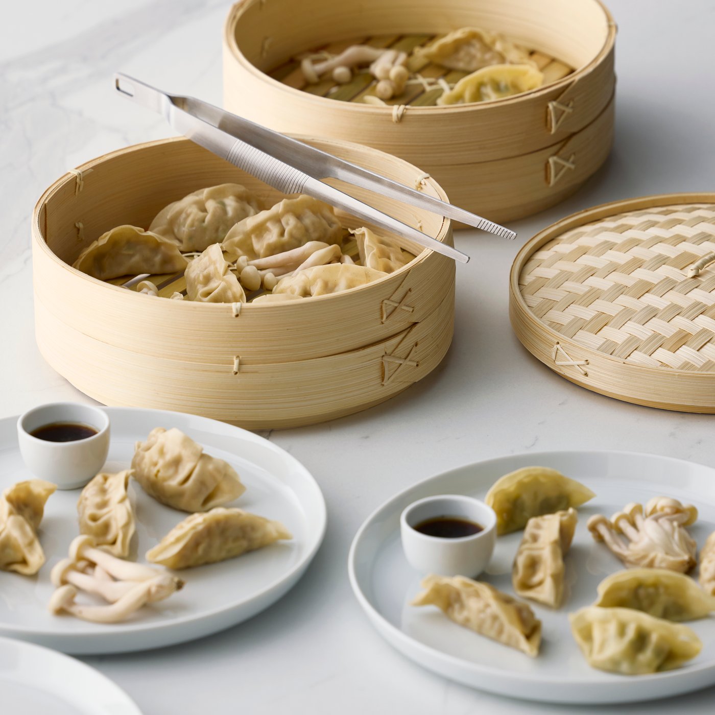 A dining setting with a bamboo KLOCKREN steamer filled with dumplings and two small bowls of dipping sauce.