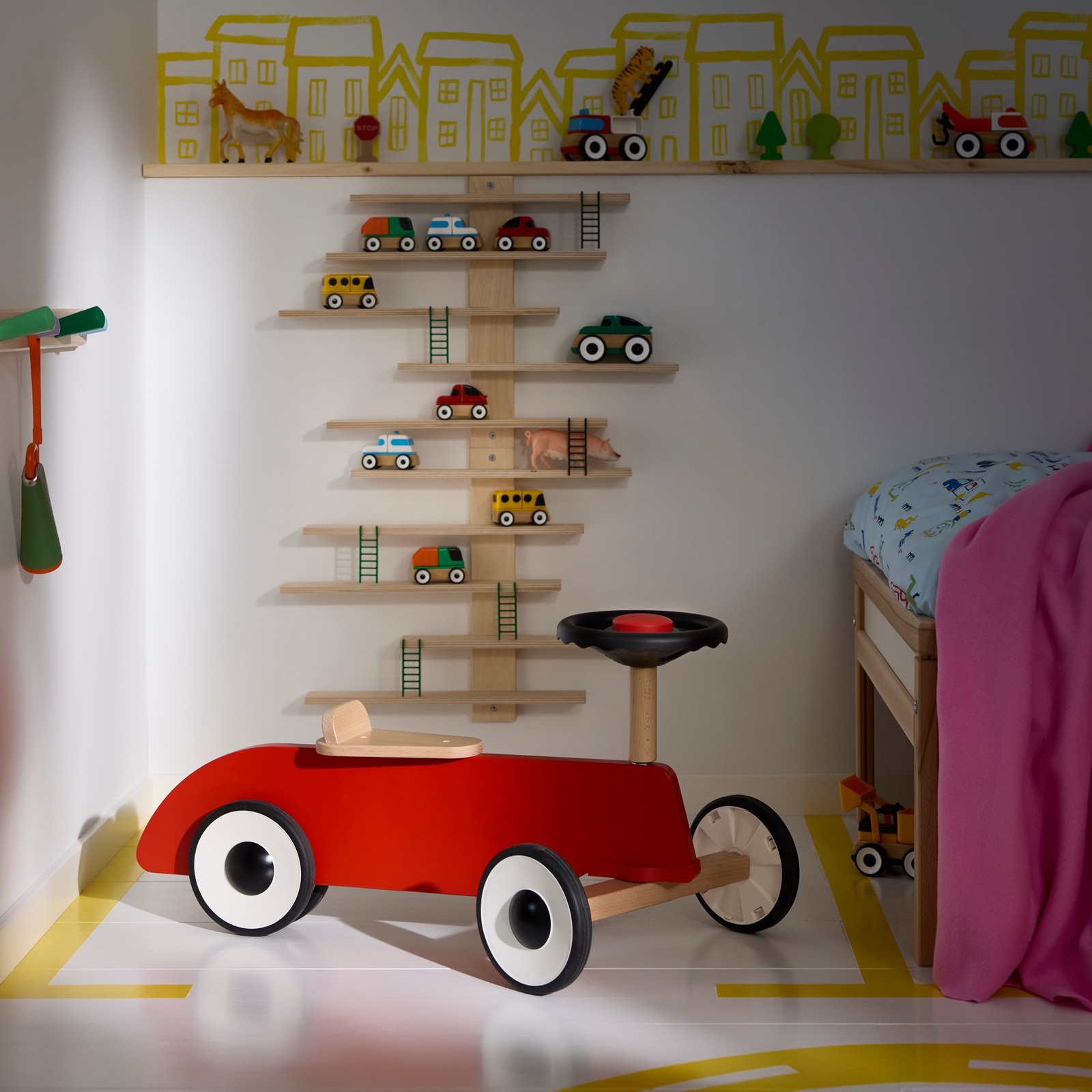 A children’s room with a FÄLTHARE ride-on toy car positioned under wall shelves holding small toys.