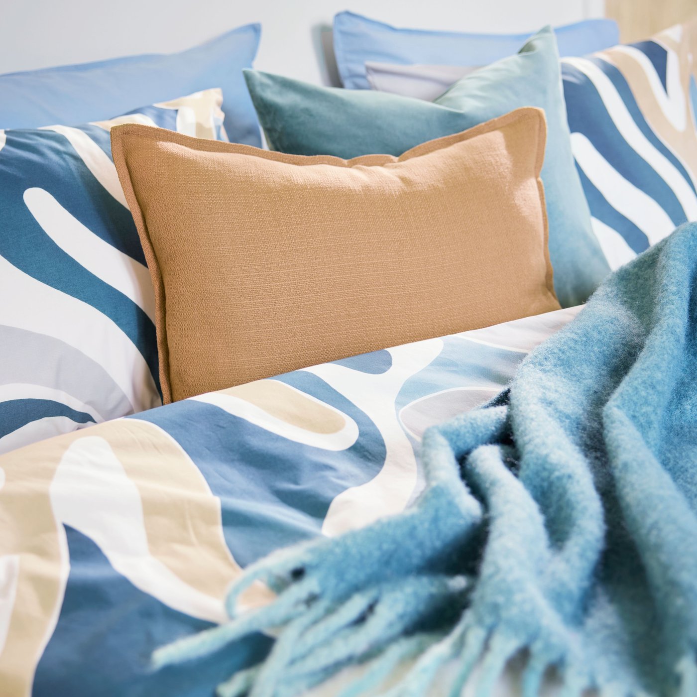 A close-up of a hotel bed with a leafy-patterned MYGGLASVINGE quilt cover and pillowcases accented by a grey-turquoise throw.