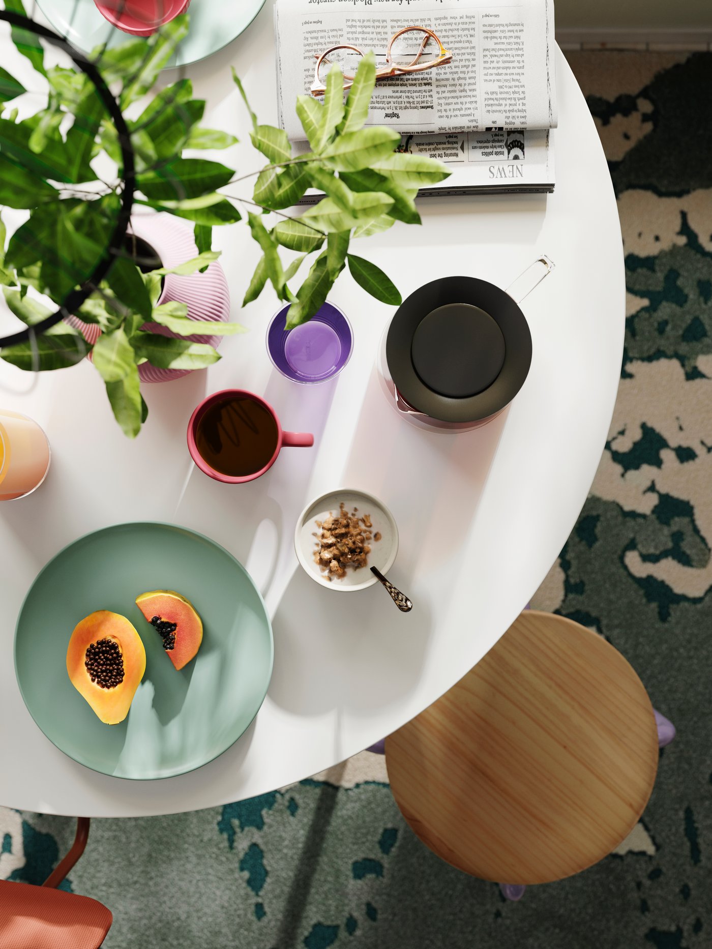 Different kinds of kitchenware are placed on a round white DOCKSTA table, seen from above, and a DOMSTEN stool is next to it.
