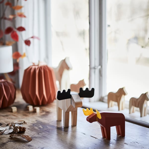 Two decorative HÖSTAGILLE moose figures are placed on a wooden table, surrounded by autumn decorations and natural light.