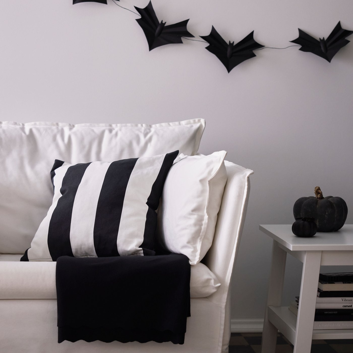 En svart- och vitrandig kudde i en vit soffa och ovanför hänger en girlang med fladdermöss.