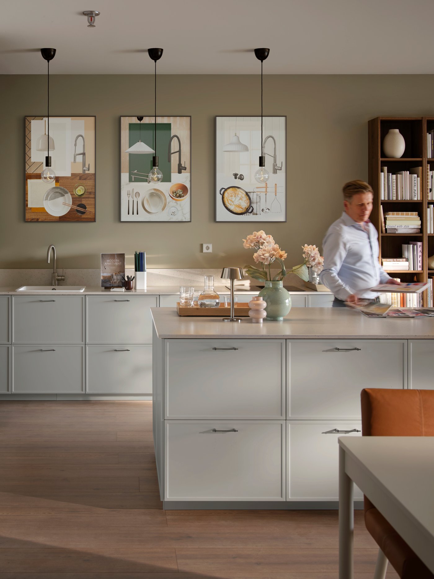 A model kitchen with light grey cabinets and built-in appliances. A man is leafing through brochures at a central island.