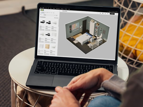 A person sitting with a laptop looking at a bedroom she has designed in IKEA Kreativ.