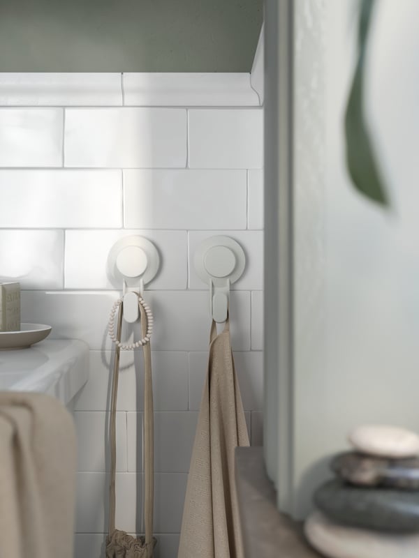 White tiled bathroom with white TISKEN towel holders on wall and beige towels hanging.