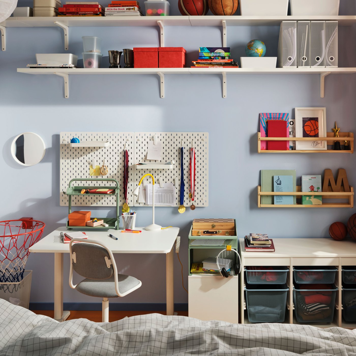 A white RELATERA sit/stand desk combination by a white TROFAST frame with six mesh storage boxes against a light blue wall.