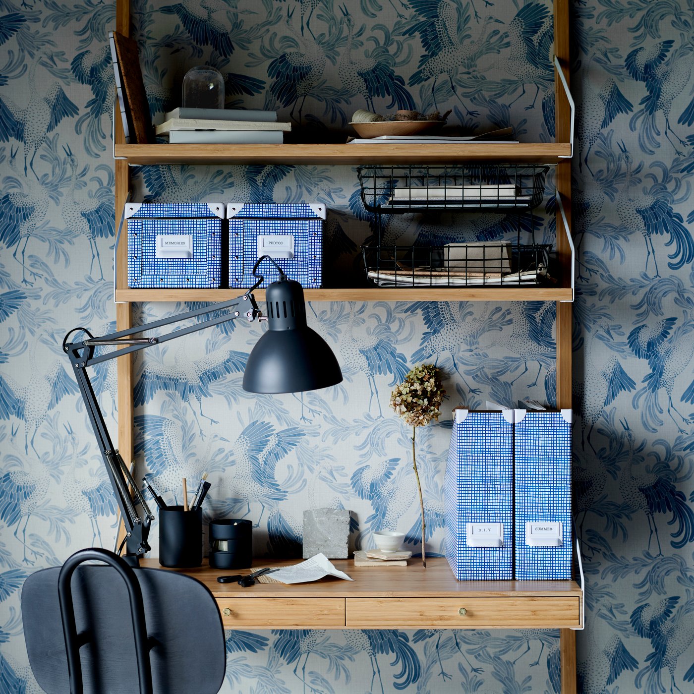 Wandregalsystem, das gleichzeitig als Schreibtisch dient. Dahinter ist gemusterte Tapete zu sehen.