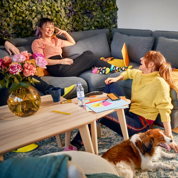 2 Personen auf einer Couch mit einem Beistelltisch, darunter ein Wollteppich aufdem ein Hund liegt.