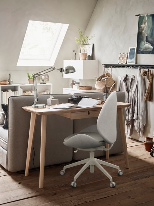 A rectangular desk with a work lamp and an office chair set under the tabletop, set against a backrest.