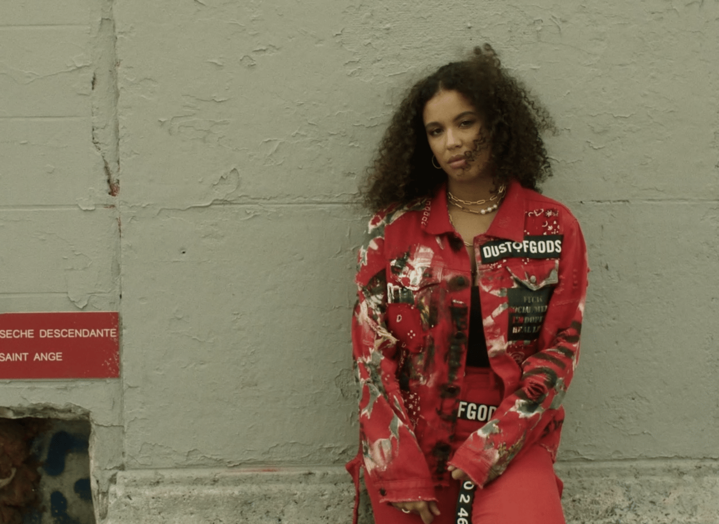 Artist Kanis u narandžastoj odeći, naslonjena uza zid.