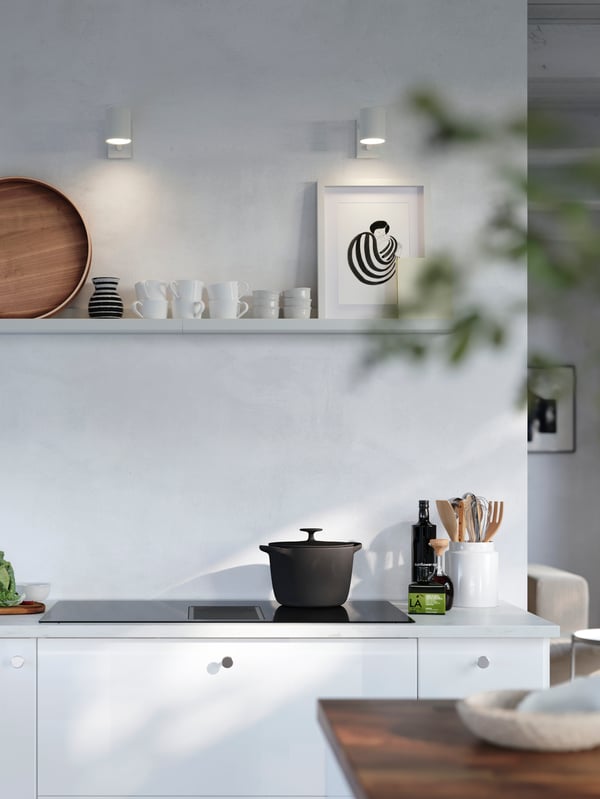 Cimaise MOSSLUNDA blanche installée sur un mur au-dessus d’une cuisinière et sur laquelle sont exposés un cadre à photo et un plateau avec des tasses.