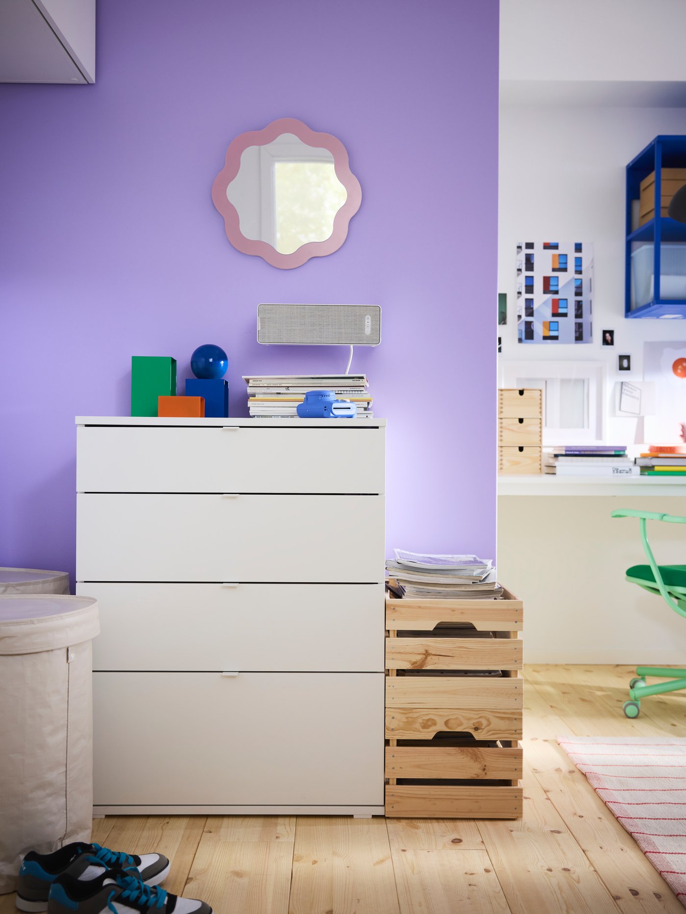 White VIHALS chest of drawers in front of a bright purple wall, with wooden boxes next to it and a round mirror on the wall.