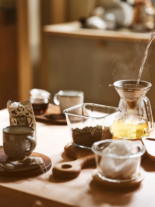 O bucătărie modernă dotată cu un recipient de mâncare din sticlă IKEA 365+, un filtru de cafea pentru cafea prin picurare, un tocător și o cană.