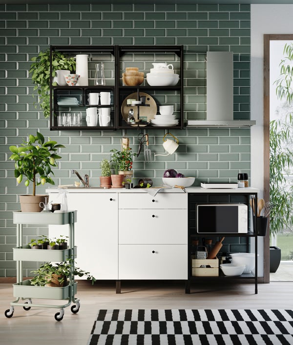 A white ENHET kitchen with open black metal frames on a green wall in a Scandinavian modern room.