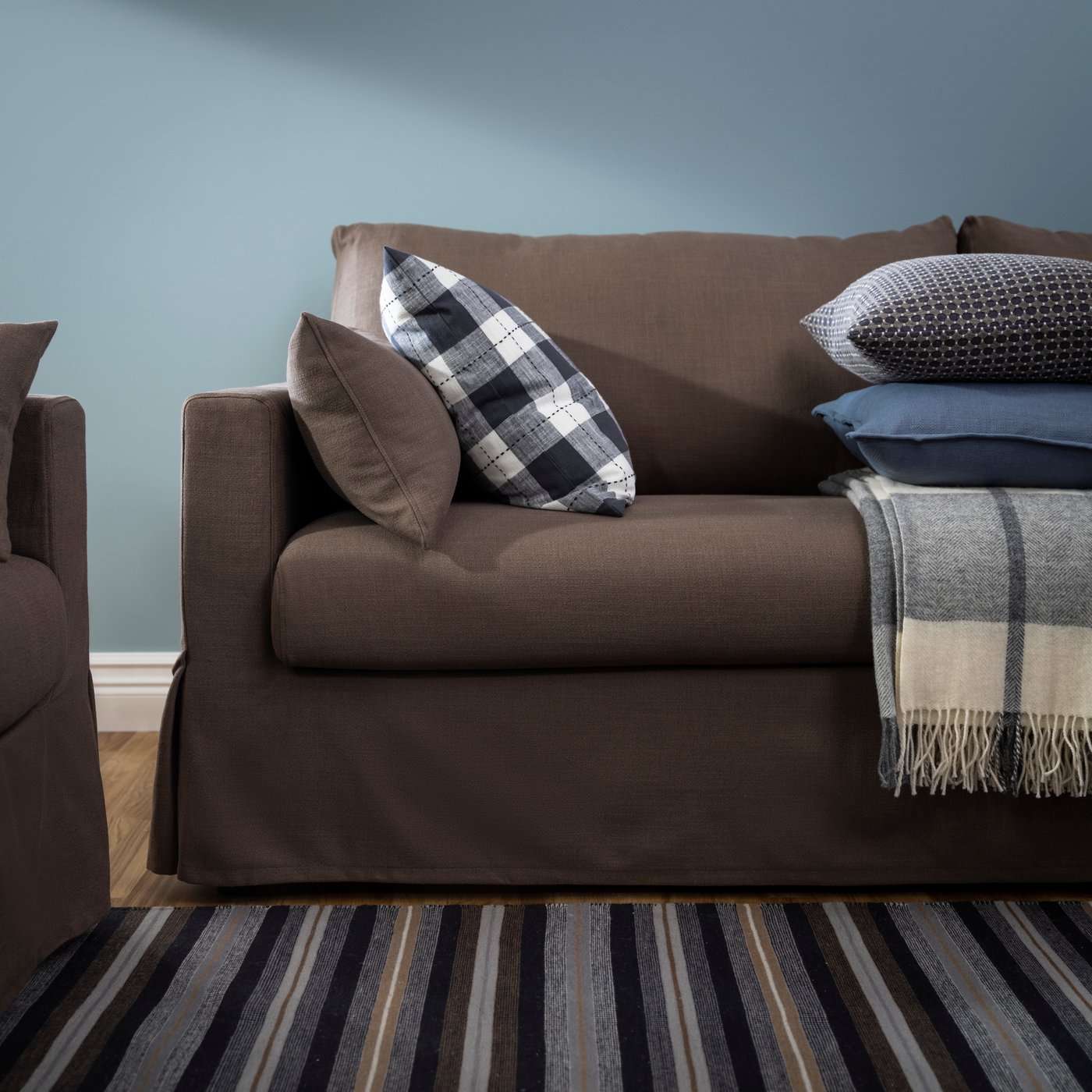A cushion with a chequered SVAMPFLY cushion cover lies on a HYLTARP 3-seat sofa near some other cushions and a throw.