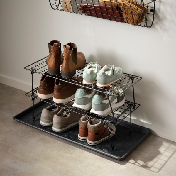 Dos zapateros GREJIG de metal negro apilados, sosteniendo zapatillas y botas sobre una bandeja en un pasillo.