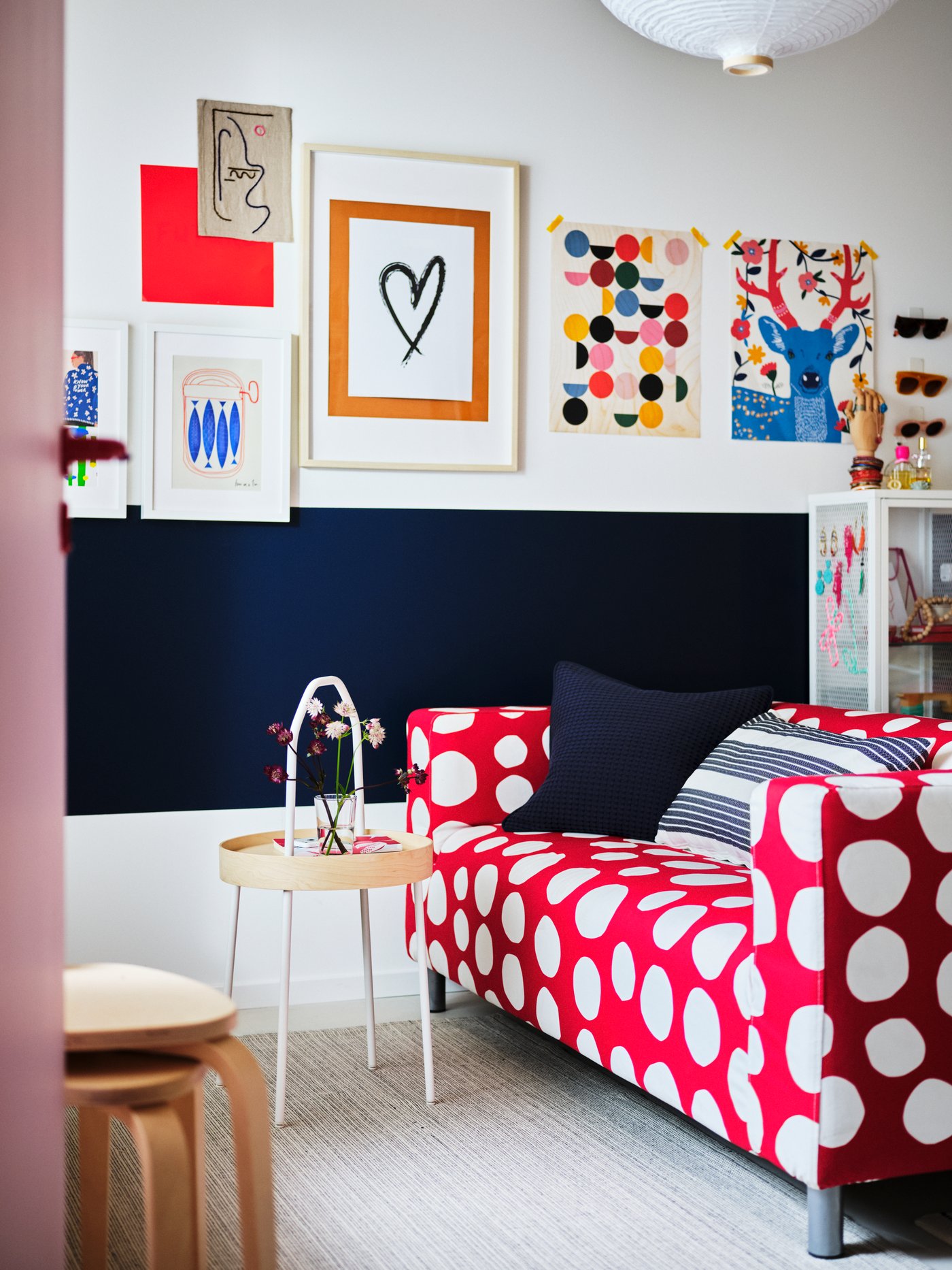 By a blue and white wall filled with art stand a red-and-white, polka-dot KLIPPAN two-seat sofa and a BURVIK side table.