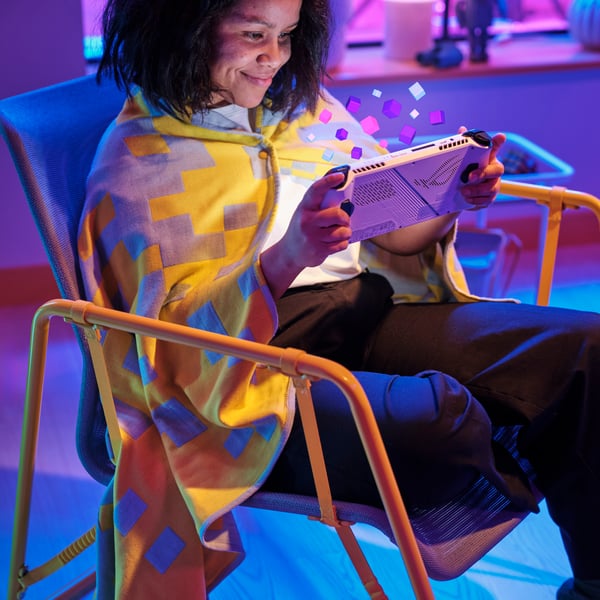 Une femme en train de jouer à la console assise sur une chaise avec un plaid jaune et gris.