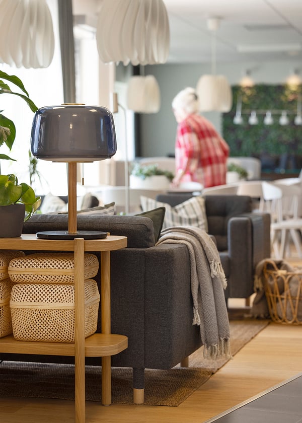 Grå LANDSKRONA 3-sits soffa med sidobord i trä med lampa och korgar.