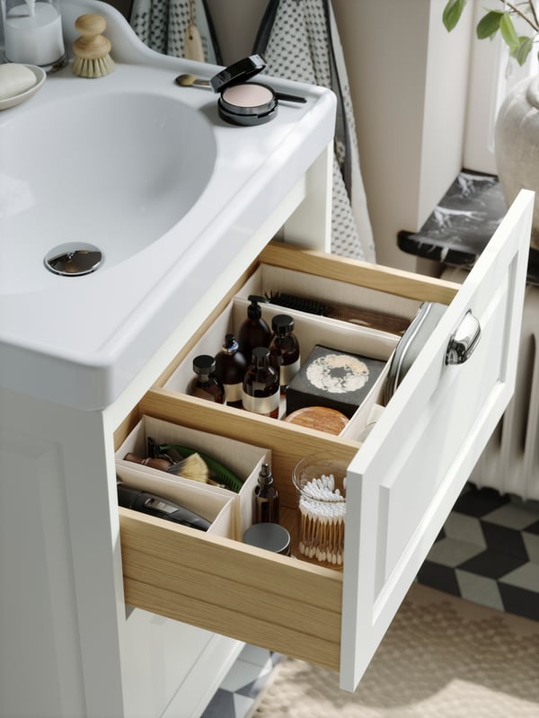 A deep TÄNNFORSEN bathroom drawer in light grey, neatly organised with BOLLÖSUND boxes inside filled with bottles and cotton pads.