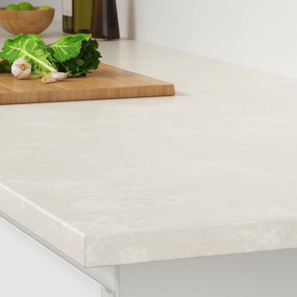 The corner of a LOCKEBO light gray white marble effect countertop on a white kitchen cabinet with a stainless steel pot on a trivet.