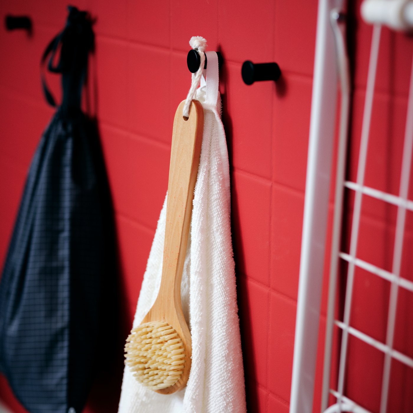 A red-tiled wall with a white VÅGSJÖN bath towel and other bathroom accessories hang from black SKOGSVIKEN hooks.