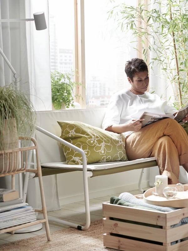 A woman sits in a room on a couch and reads a newspaper.