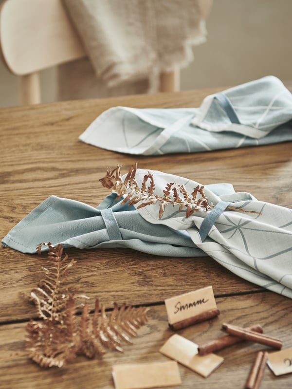 A wooden traditional table with napkins placed on top being tied together for a table setting. 