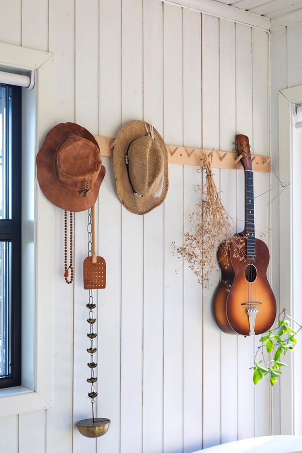På en knagg i tre henger to hatter i strå, gitar og dekorative gjenstander.