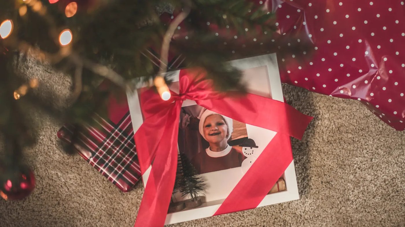 En vit IKEA RIBBA ram med presentband runt under en gran tillsammans med andra inslagna paket.