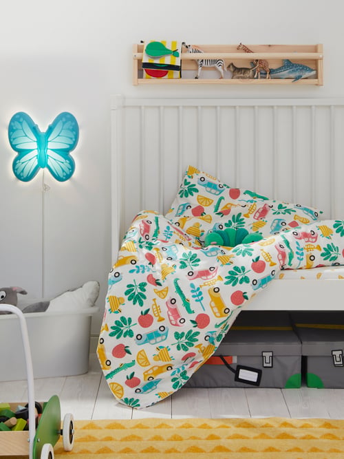 A GULLIVER crib with RÖRANDE bed linen sits under FLISAT wall storage and near a blue UPPLYST LED wall lamp.