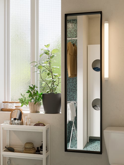 O baie modernă cu o oglindă dreptunghiulară, o lampă oglindă pe perete LED, un cărucior alb și un set de cinci borcane cu capace.