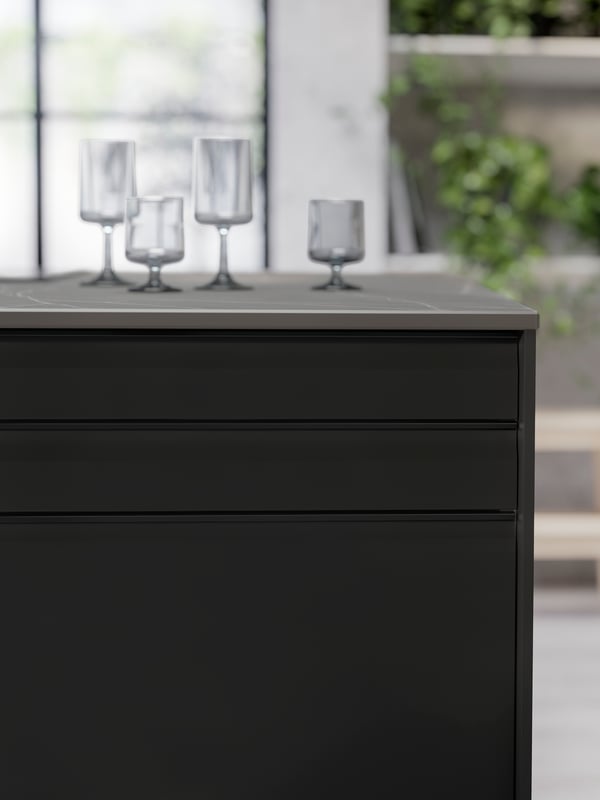 A SKARARP worktop in matte black and brown marble effect with wine glasses on it and UPPLÖV anthracite kitchen fronts.