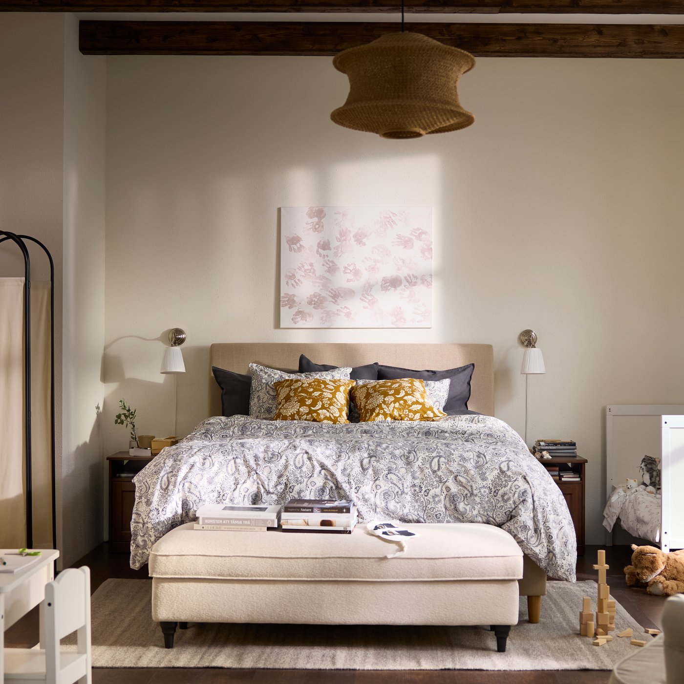 Bedroom in all beige and white with a children’s bed next to the grown-up’s bed, and an armchair in the foreground.
