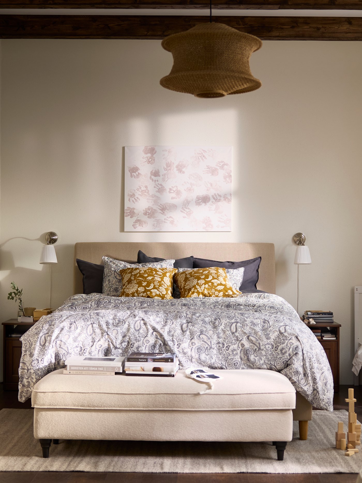 Es ist ein Schlafzimmer in Beige und Weiß mit einem Kinderbett neben dem Elternbett zu sehen. Im Vordergrund steht ein Sessel.