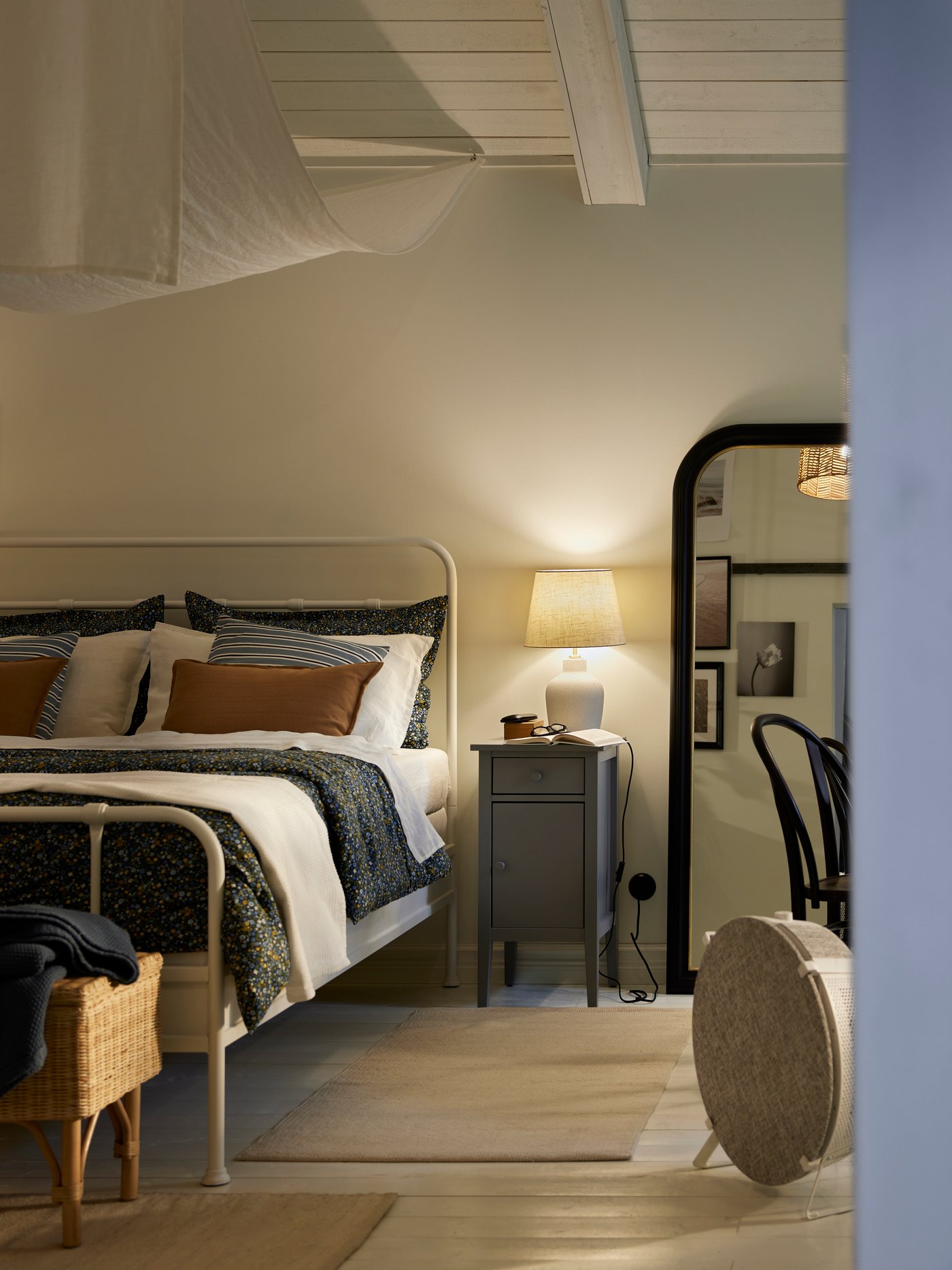 A grey nightstand with a lamp on it beside a white STJÄRNÖ bed. A white STARKVIND air purifier is by the end of the bed.