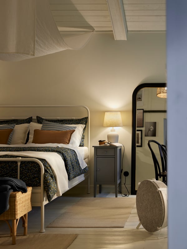 A grey bedside cabinet with a lamp on it beside a white STJÄRNÖ bed. A white STARKVIND air purifier is by the end of the bed.