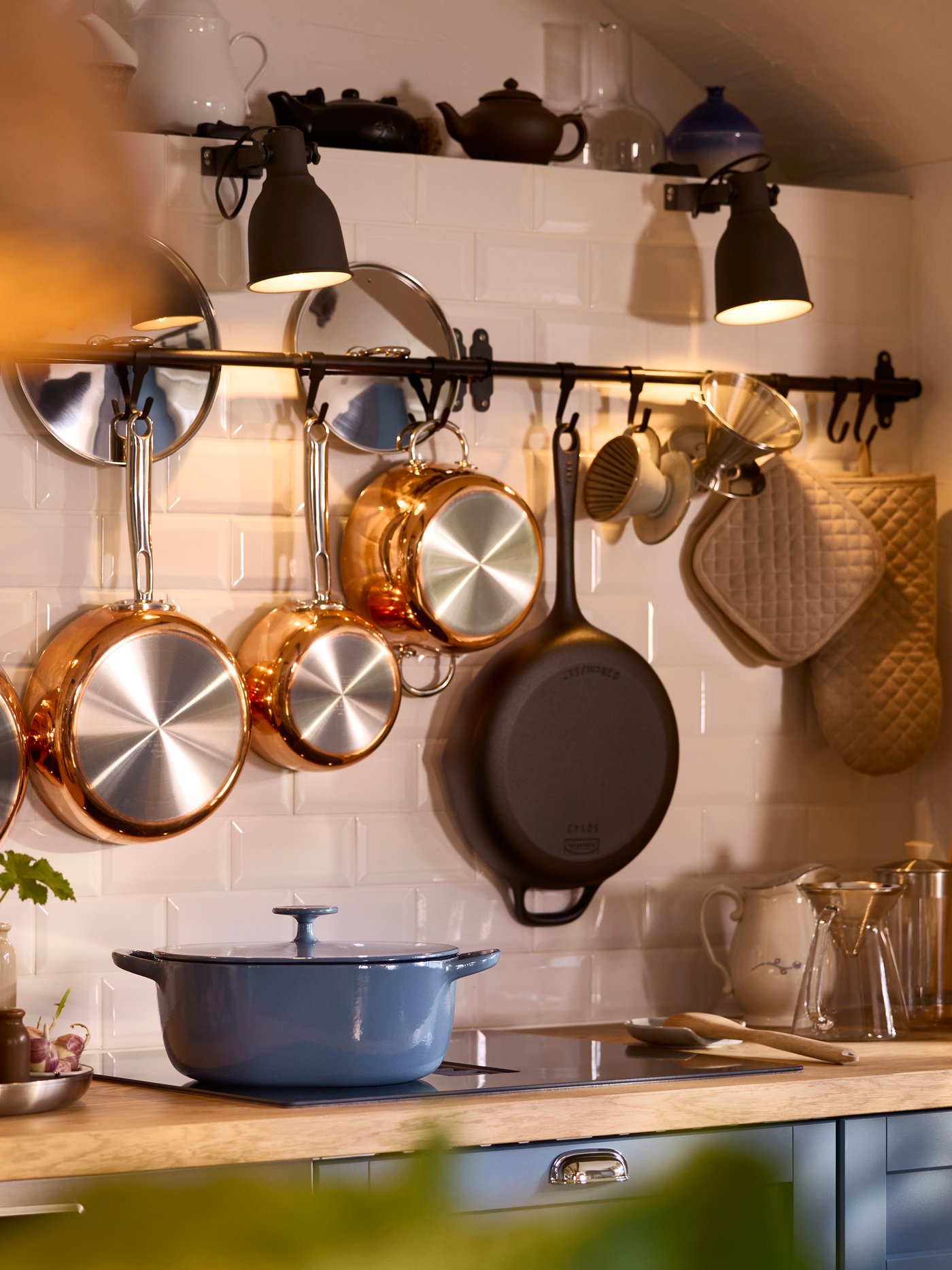 A HULTARP rail is attached to a kitchen wall and there are pots and pans hanging from hooks attached to it for a rustic look.