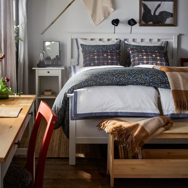 Een zonovergoten slaapkamer met een netjes opgemaakt bed en gedecoreerd met een MYRHULL plaid en HEMNES en een nachtkastje.