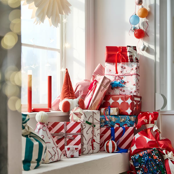 A stack of gifts wrapped in VINTERFINT wrapping paper on a windowsill beside a VINTERFINT Santa soft toy.