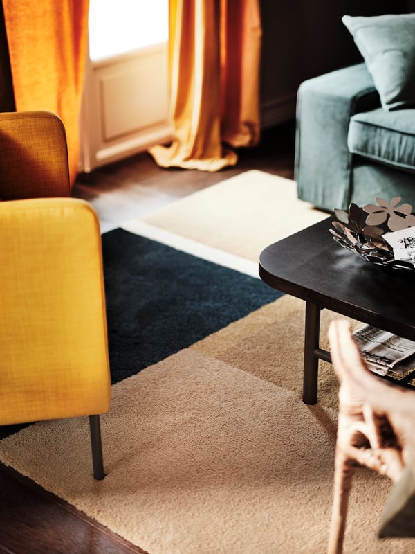 A sofa, coffee table and two armchairs on and around a yellow-brown/dark blue low pile SKRIFTSPRÅK rug.