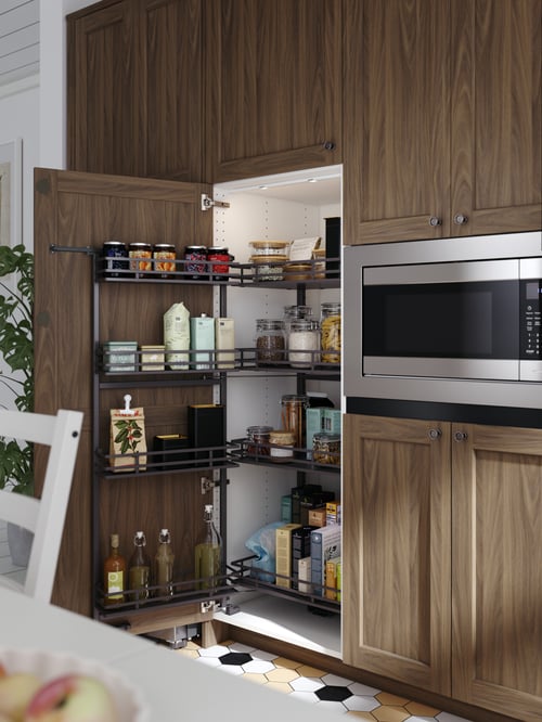 A high kitchen cabinet containing a UTTRUSTA pull-out larder filled with different types of food in containers and bottles.