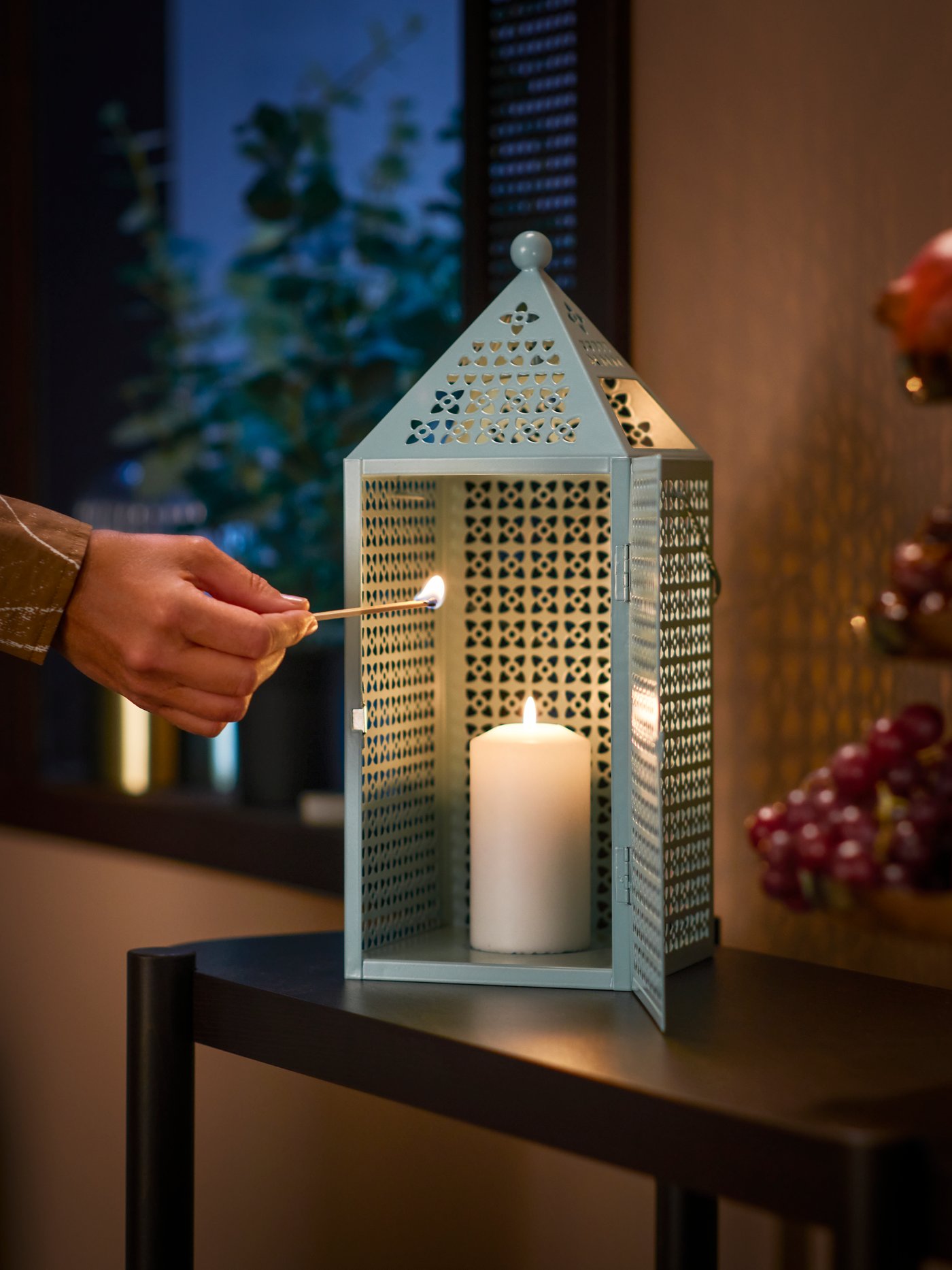Tangan memegang mancis sambil menyalakan lilin dalam lantera GOKVÄLLÅ.