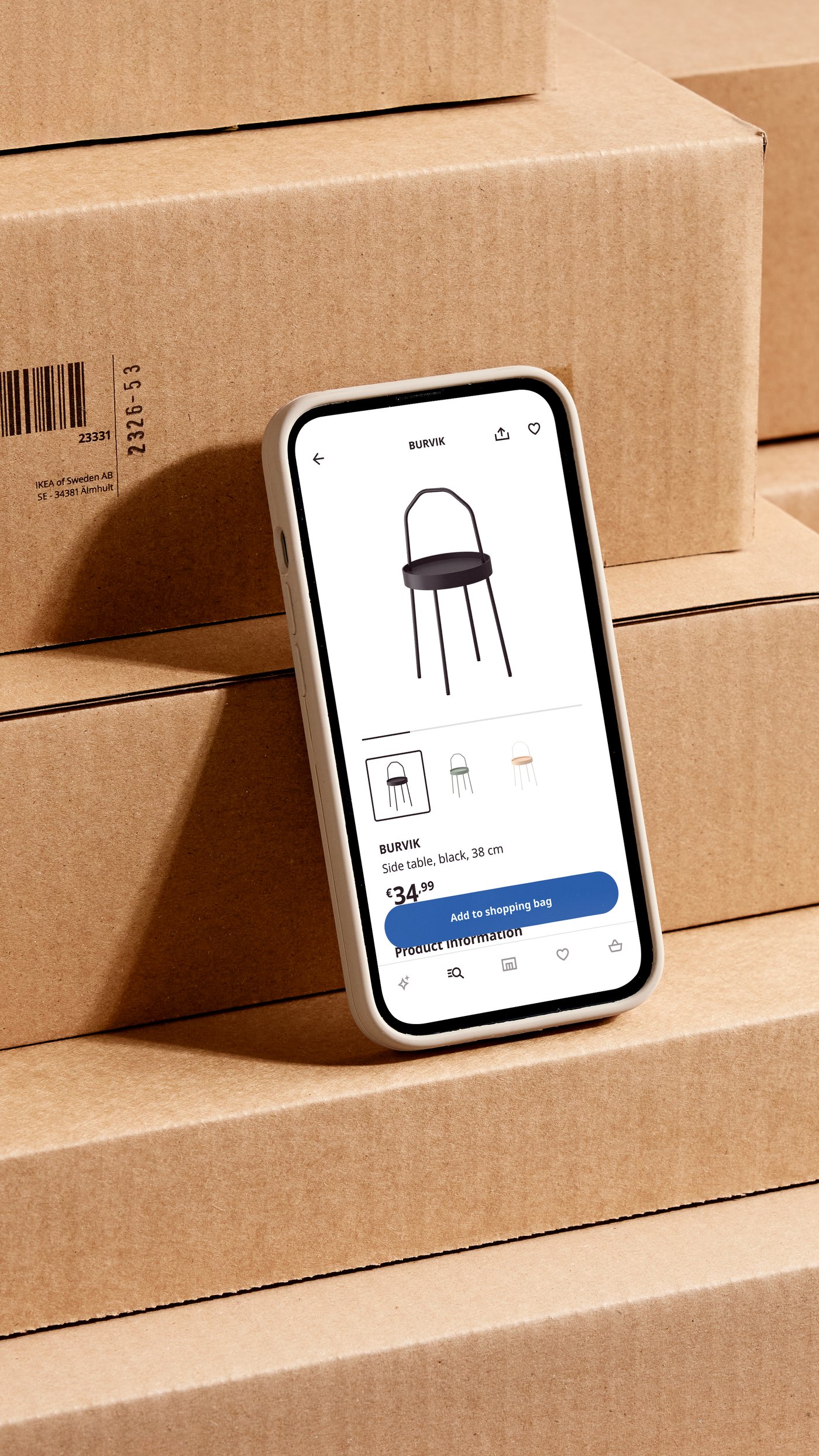 A smartphone leaning against stacked flatpacks displays a product page in the IKEA app.