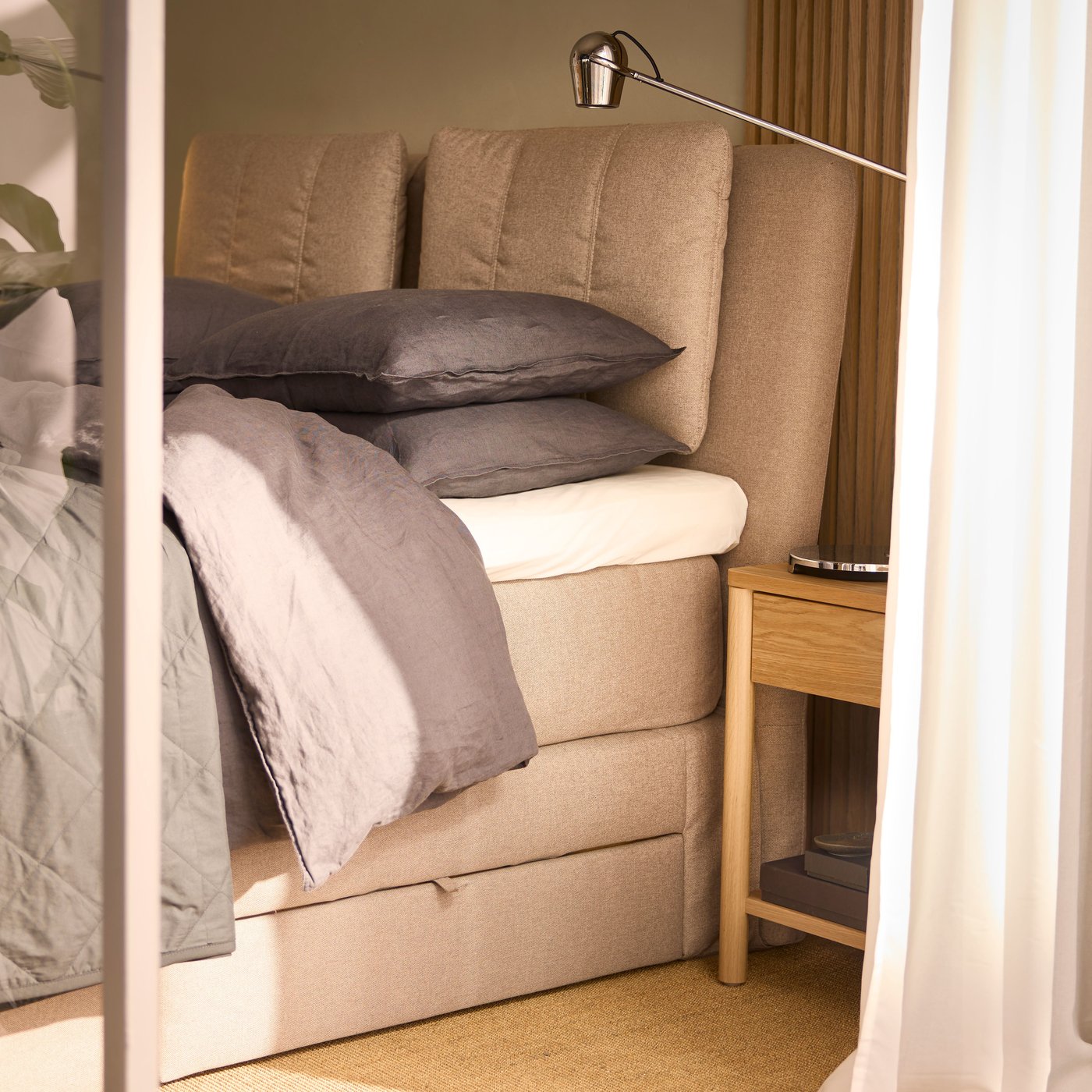 Es ist ein beigefarbenes LILLFJÄLLET Boxspringbett mit Bettkasten zu sehen, auf dem Bettzeug in dunkelgrauer DYTÅG Bettwäsche liegt.