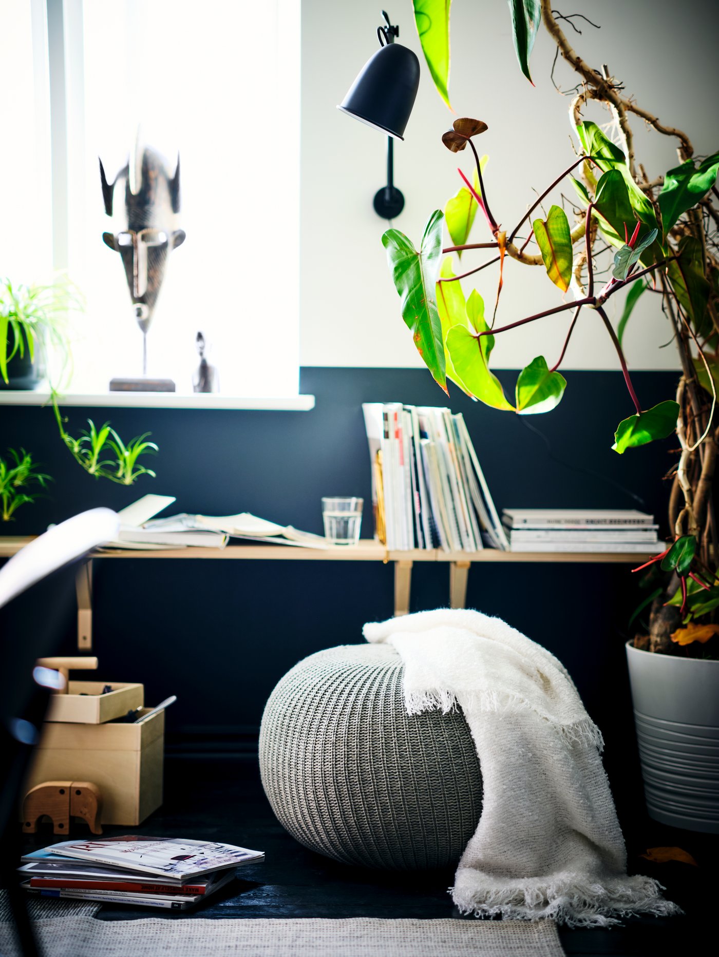 An area beneath a sunlit window with a SANDARED pouffe, a wall shelf with magazines and plants.