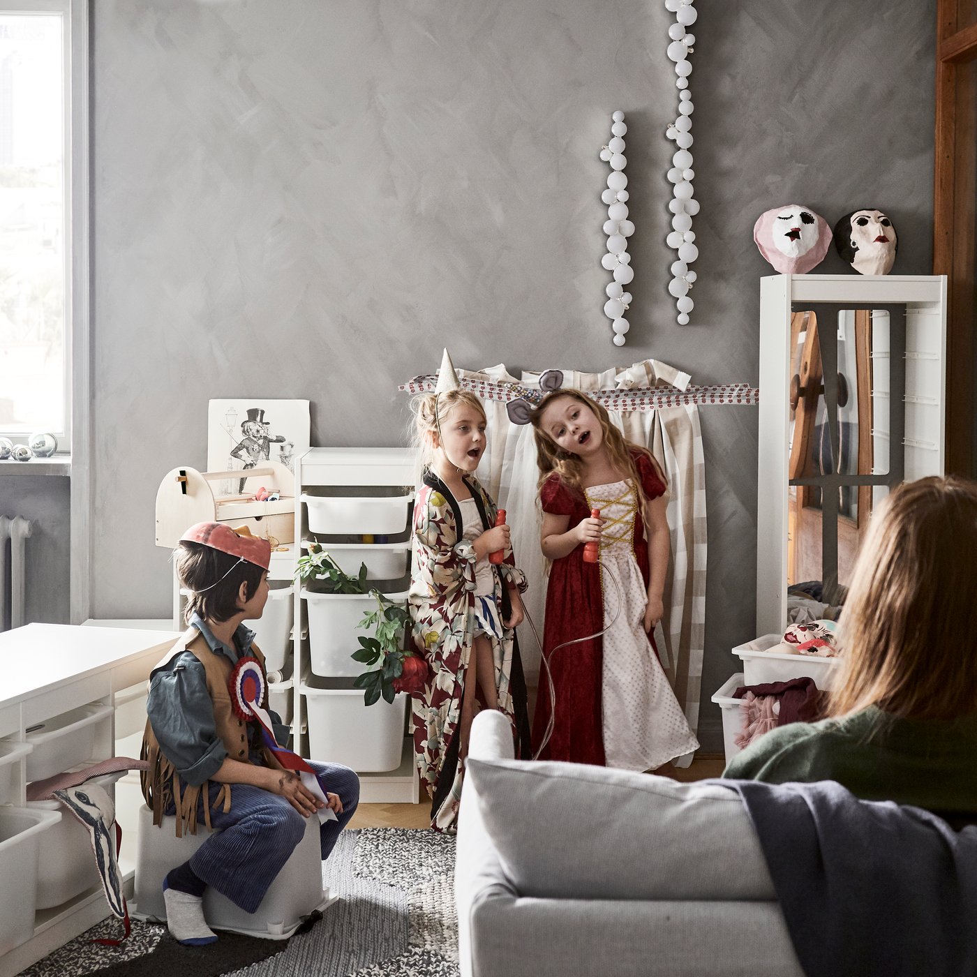 Två barn står utklädda med ett hopprep i händerna som en mikrofon och uppträder för ett barn utklädd till cowboy och en vuxen som sitter i en soffa.