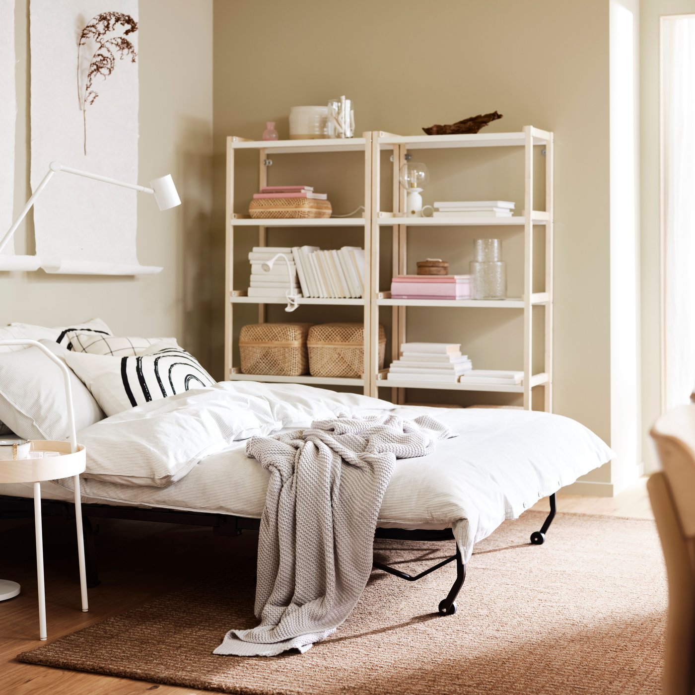 LYCKSELE HÅVET sofa-bed turned into double bed with white bedding and two bookcases behind it.